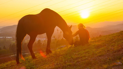 LENS FLARE: Loving girl petting her horse while it grazes in the sunny pasture. © helivideo
