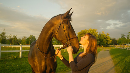 Obraz premium CLOSE UP: Cheerful young woman holds her horse's reins and looks at it lovingly.