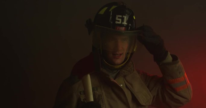 Firefighter looking at camera puts down visor and turns towards smoke - slow motion