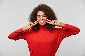 Close up of an happy young girl showing peace gesture. African American smiling woman with afro hairstyle looking at camera and doing victory signs with fingers. Isolated over white background