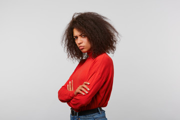 Offended upset latino woman with afro hairstyle in a red longsleeve standing sideways with hands...