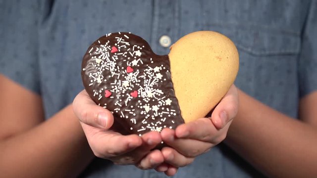 Closeup front view of cute small hands of young kid holding special sweet cookie in shape of heart. Happy Valentine day oy Mothres day holiday celebration concept. Real time 4k video footage.