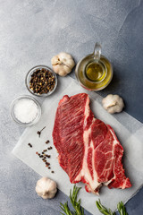 Close up fresh beef meat with oil, herbs and spices on gray background. Top view free space