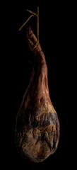 Whole leg of Spanish Iberian serrano ham hanging on a rope. On black background