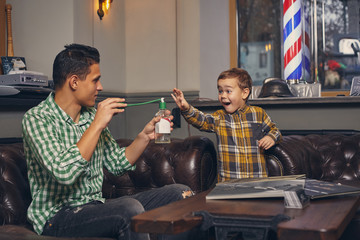 Young father and his stylish little son in the barbershop in the waiting room.