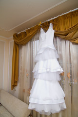 white bride dress hanging on a hanger in the room by the window without people