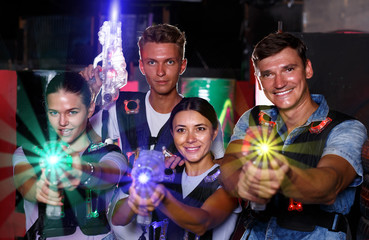 Young friends posing with colored laser guns  in dark labyrinth