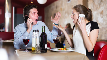 Emotional couple visitors at restaurant speaking on phones