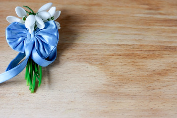 Obraz na płótnie Canvas A small bouquet of beautiful white snowdrops tied with a blue ribbon with a silk bow on a wooden background.