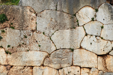 Background - ancient Greek rock wall with weeds and moss growing in cracks and wildflowers in one corner