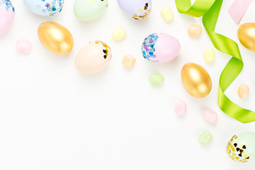 Festive Happy Easter background with decorated eggs, flowers, candy and ribbons in pastel colors on white. Copy space
