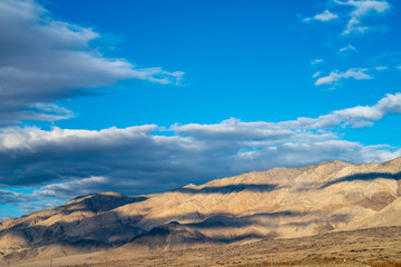 blue sky white clouds cast shadows over light tone desert hills in Eastern Sierra Nevada, California, USA