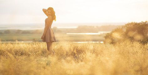 dreamy girl in a field at sunset, a young woman in a haze from the sun enjoying nature, romantic style