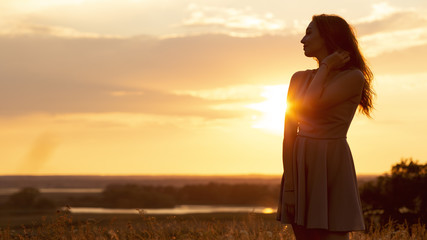 silhouette of dreamy girl in a field at sunset, a young woman in a haze from the sun enjoying...