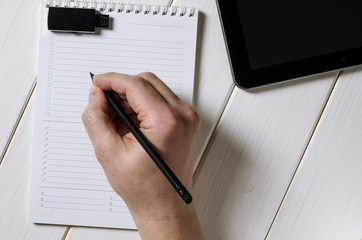 Man hands writing notes to the notebook on wooden table in home office