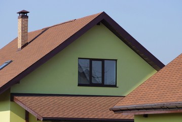 green attic of a house with a window and brown tile on the roof against a blue sky