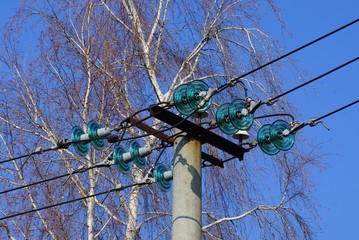 part of a gray concrete pillar with electrical wires against a blue sky and tree branches