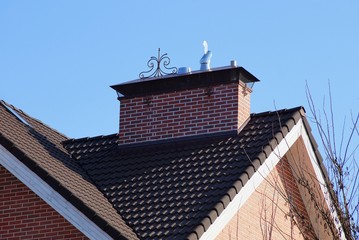 brick chimney on the roof with brown tile against a blue sky