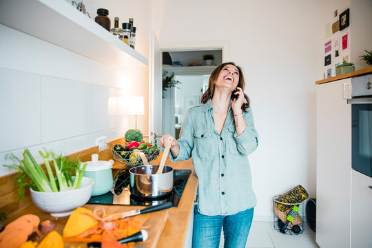 Laughing woman talking on the phone, while preparing pumpkin soup