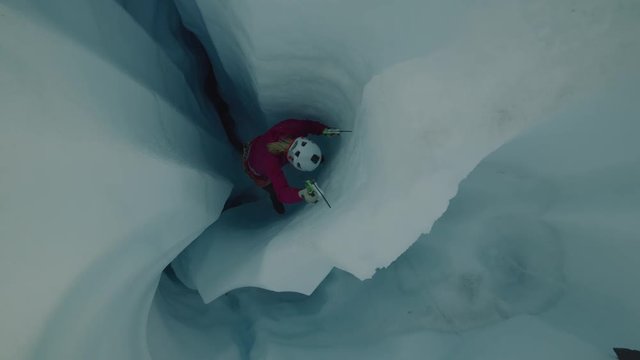 High angle view of ice climber ascending narrow crevice on glacier using hooks / Palmer, Alaska, United States