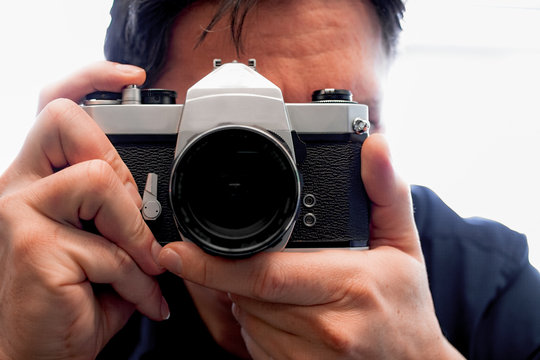 Photographer holding a old film photo camera  on is hand in front of is face