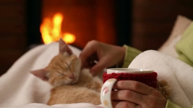 Woman sitting at the fireplace with a cup of coffee and her orange tabby kitten - camera slide, refocus
