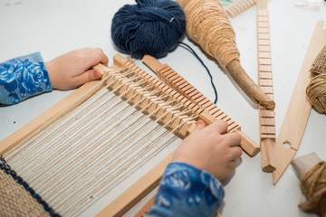 A little girl learns process to thick threads. Creating a picture by weaving.