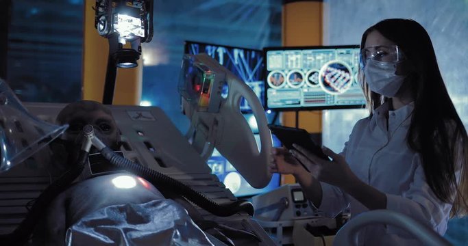 Beautiful female scientist fixes surveillance devices on an alien. Space alien lying on the operating table in the laboratory.