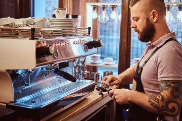 Side view of a barista cleans the portafilter before preparing the cappuccino in a coffee shop or restaurant.