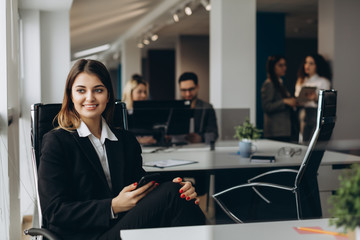 Fototapeta premium Smiling business woman using cell phone with colleagues on background in office.