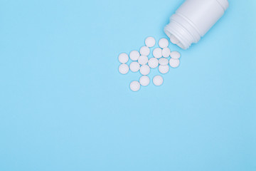 Medicinal and prescription white pills flat background.Copy space. White medicine jar and white pills scattered on pastel blue background. Concept of application of athybiotics.