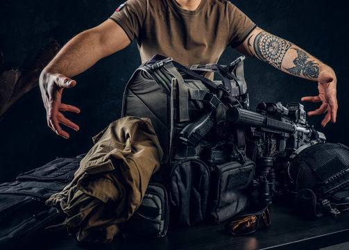 Casually dressed man showing his military uniform and equipment. Modern special forces equipment. Studio photo against a dark textured wall
