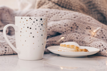 Warm cozy knitwear and a cup of coffee with a cake on white marble windowsill against white window background. Copy space.