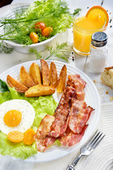 Food on the table. Breakfast with bacon. Fried bacon with. French fries and tender egg, and a glass of fresh juice.
