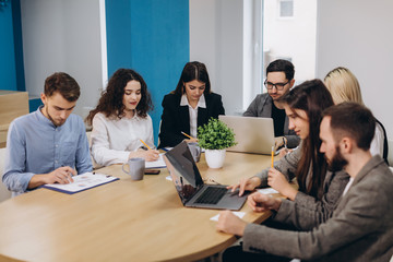 Multi ethnic people entrepreneur, small business concept. Woman showing coworkers something on laptop computer as they gather around a conference table.