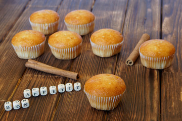 Fresh golden muffins with cinnamon sticks lie on a wooden surface made of pine boards. Bon appetite. Tasty and healthy food