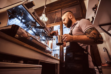 Low angle photo of a stylish tattooed barista working on a coffee machine in a coffee shop or restaurant