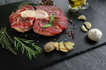 Raw Osso Buco steak on a black stone surrounded by spices