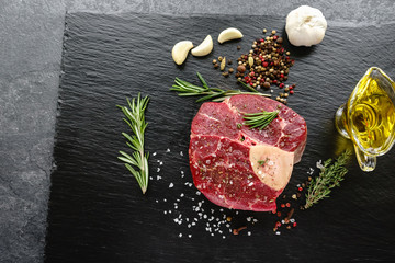 Raw Osso Buco steak on a black stone surrounded by spices
