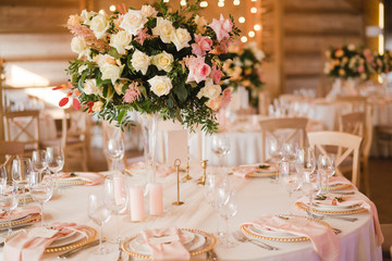 Coziness and style. Modern event design. Table setting at wedding reception. Floral compositions with beautiful flowers and greenery, candles, laying and plates on decorated table.