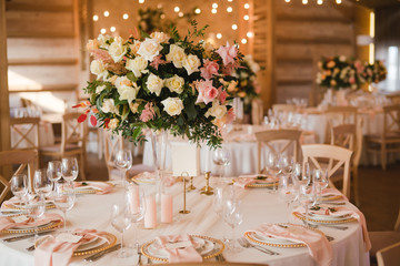 Coziness and style. Modern event design. Table setting at wedding reception. Floral compositions with beautiful flowers and greenery, candles, laying and plates on decorated table.