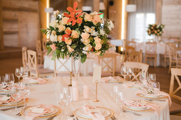 Coziness and style. Modern event design. Table setting at wedding reception. Floral compositions with beautiful flowers and greenery, candles, laying and plates on decorated table.
