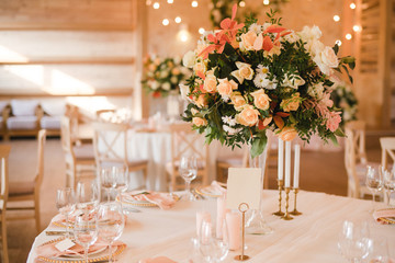 Coziness and style. Modern event design. Table setting at wedding reception. Floral compositions with beautiful flowers and greenery, candles, laying and plates on decorated table.