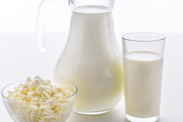 Fresh milk in a glass and jug with a bowl of cottage cheese on a white background. Dairy products in the morning for breakfast are very useful for children's health.