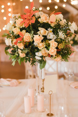 Coziness and style. Modern event design. Table setting at wedding reception. Floral compositions with beautiful flowers and greenery, candles, laying and plates on decorated table.