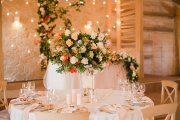 Coziness and style. Modern event design. Table setting at wedding reception. Floral compositions with beautiful flowers and greenery, candles, laying and plates on decorated table.