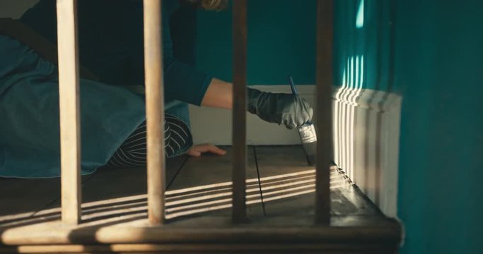 Young woman applying wood stainer to the floorboards