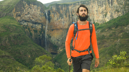 Man climbing hill walking stick in hand and backpack, Waterfall of Tabuleiro in the background