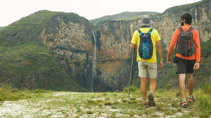 Man climbing hill walking stick in hand and backpack, Waterfall of Tabuleiro in the background