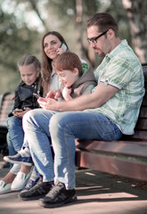 parents and children using their smartphones sitting on a Park bench.